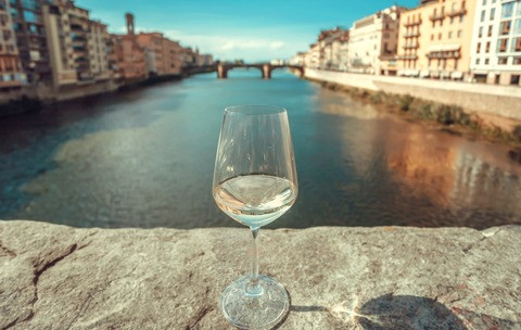 Traveling around Italy with wine glass. Old buildings of Florence with river and ancient cityscape in Italy